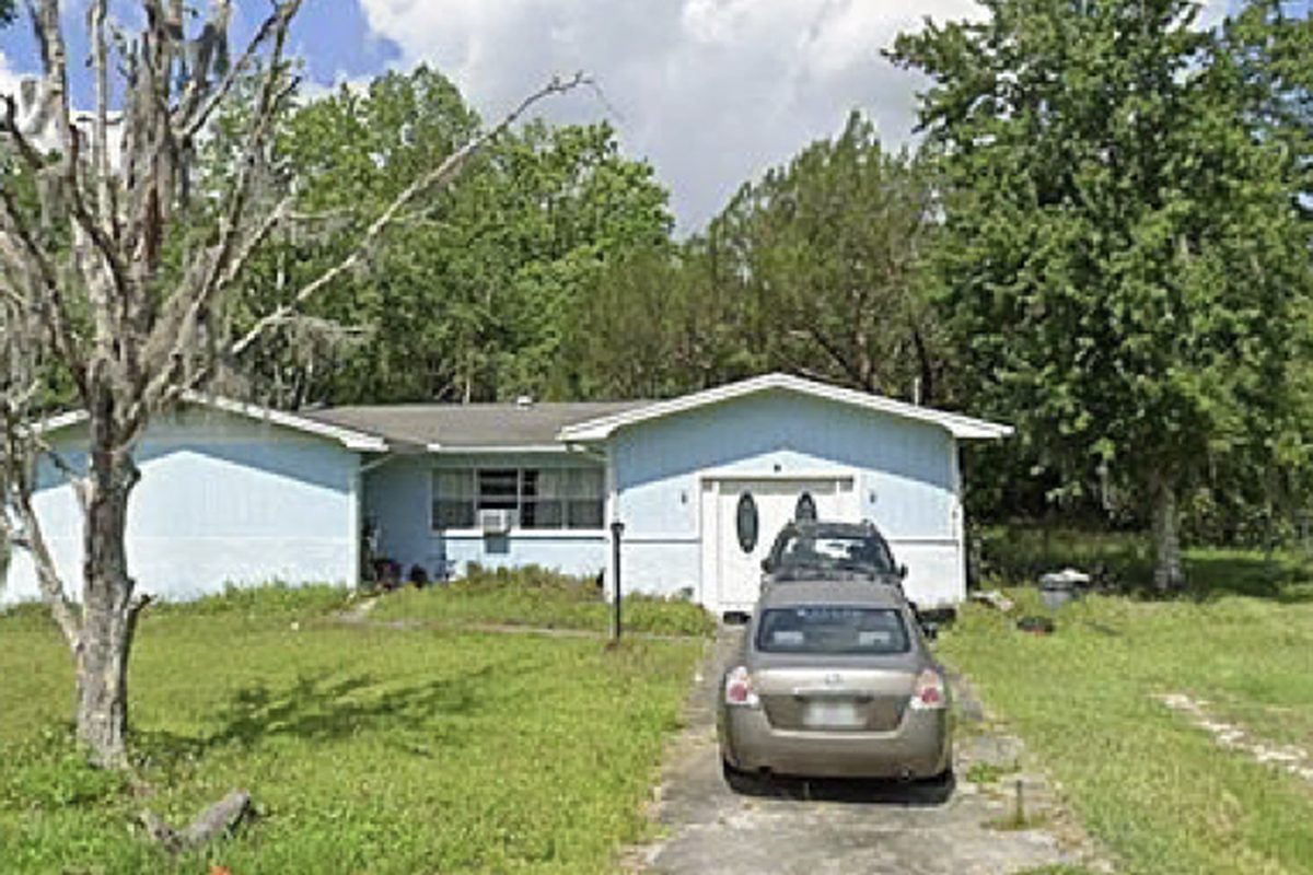 Pale blue ranch home with window air conditioners and dead trees in the yard, as found before purchase