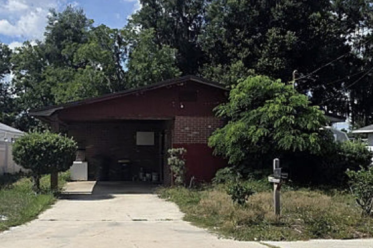 Block ranch with an attached carport, overgrown yard and stored belongings, as found before purchase