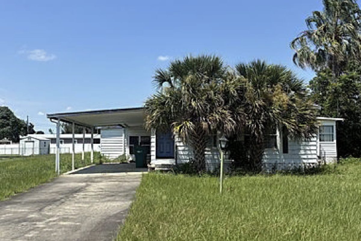 White manufactured home with a carport and knee-high grass, as found before purchase