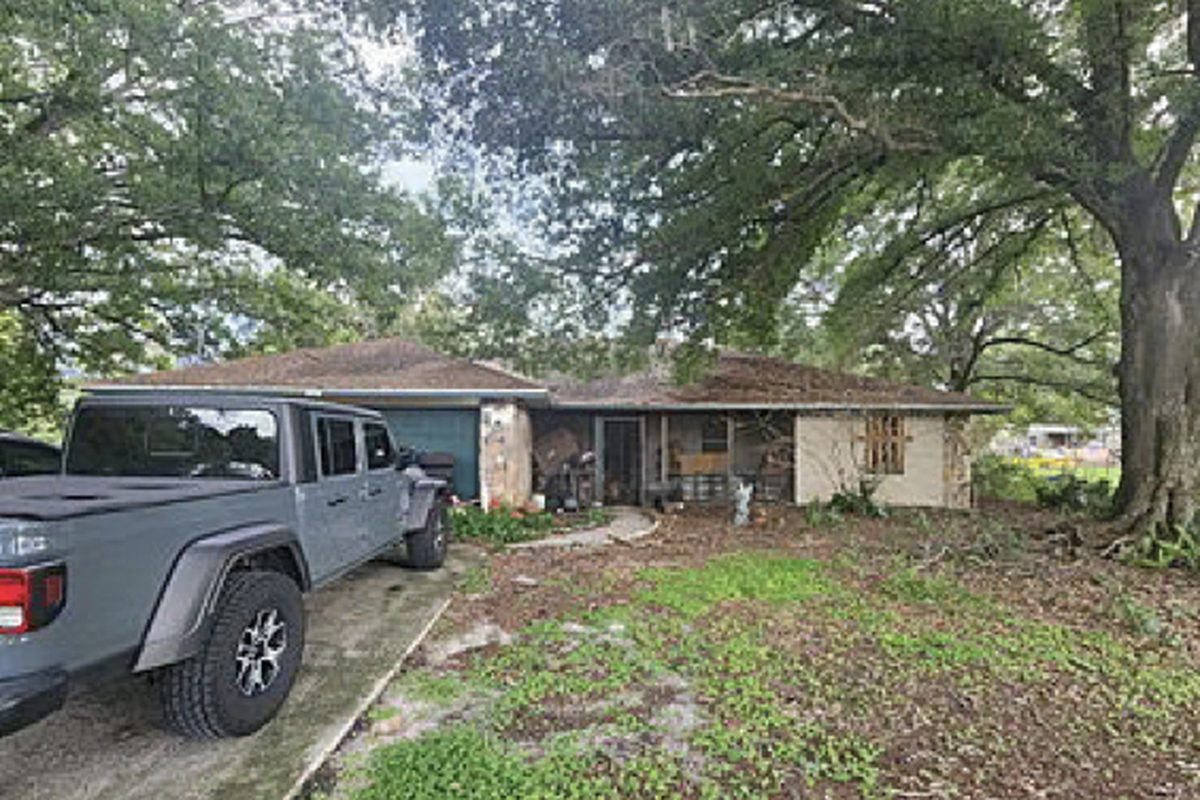 Single-storey ranch under mature oaks with a damaged front porch and bare yard, as found before purchase