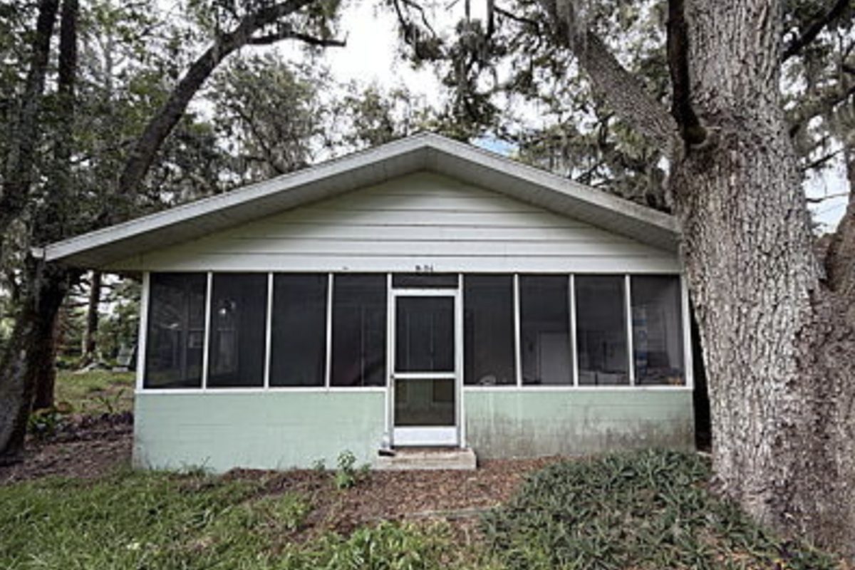 Mint green block house with a full-width screened porch and weathered exterior, as found before purchase