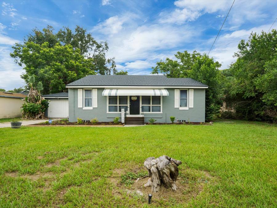 Renovated blue stucco bungalow with striped awning and fresh landscaping